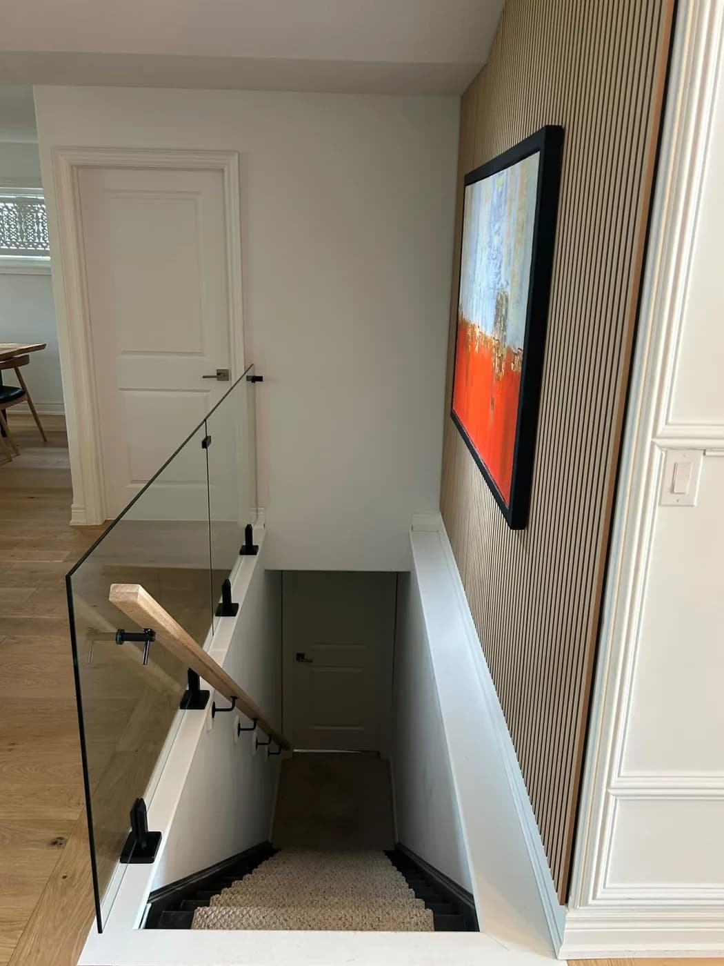 Glass stair railing with a wood handrail on a staircase down to a finished lower level
