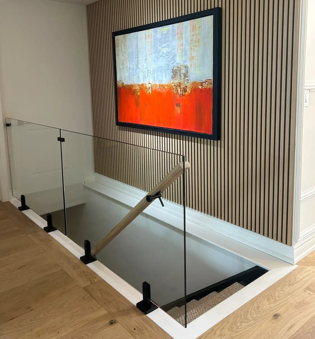 Frameless glass panels with black standoffs and a raked oak handrail at a stair opening